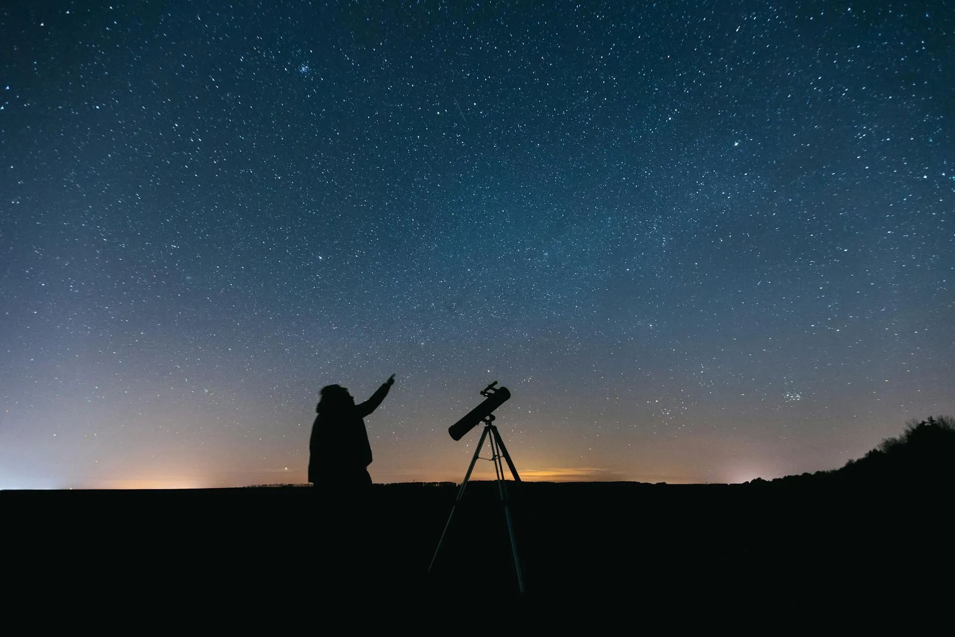 Silhouette of a person with a telescope gazing at the starry night sky